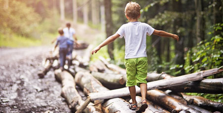 Children walking on fallen trees in the woods.