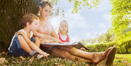 A woman reading to her children in an outdoor setting.